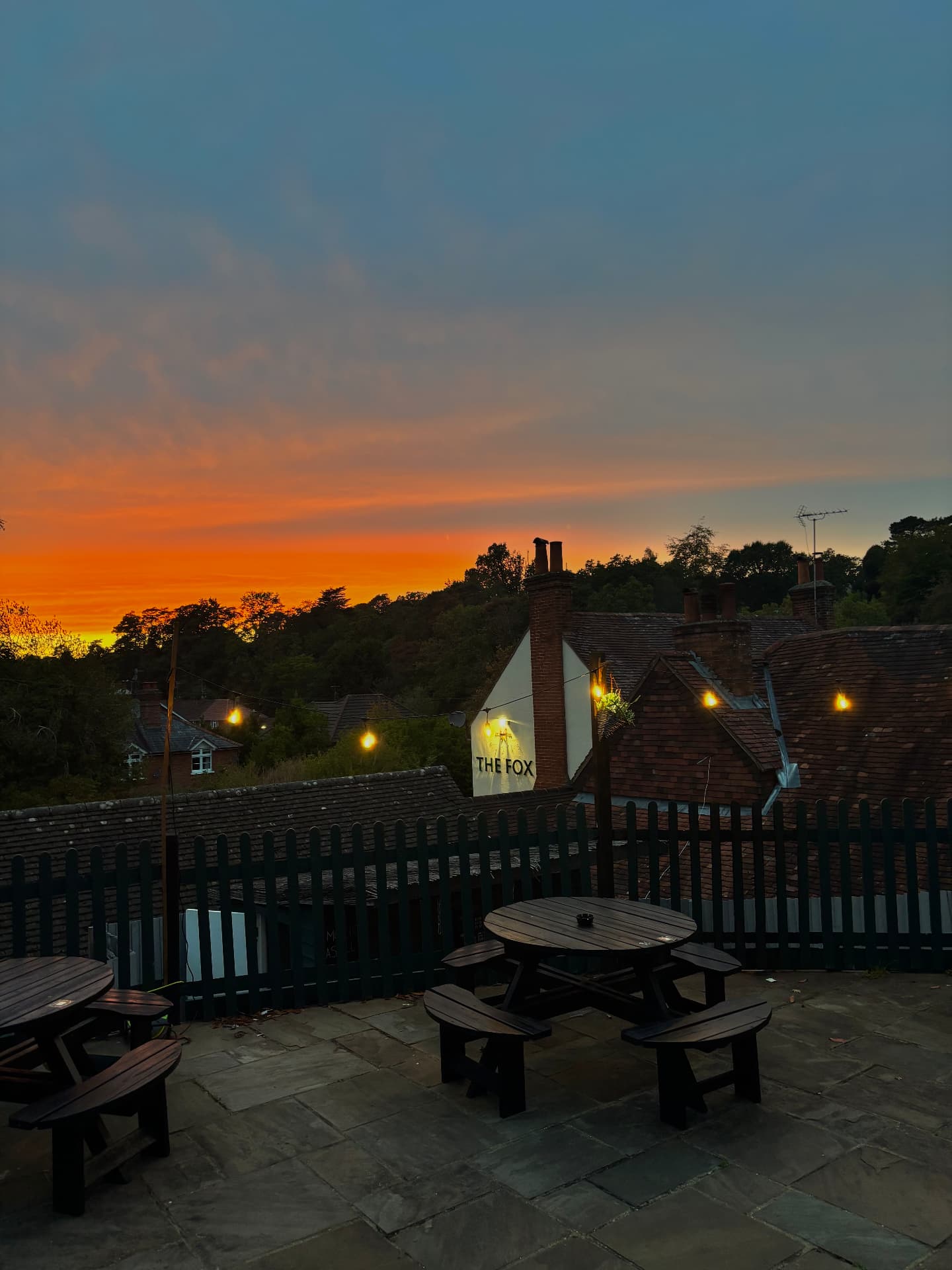 Sunset over The Fox's terrace, with festoon lights and picnic benches